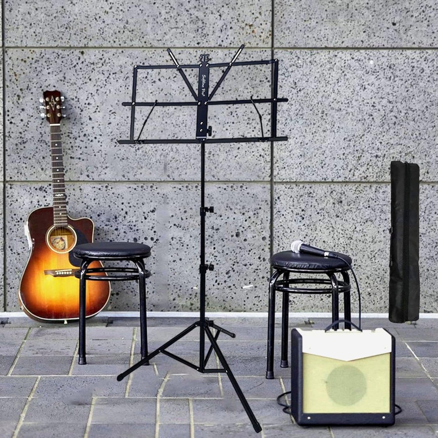 Guitar, music stand, amplifier, and stools against a stone wall.