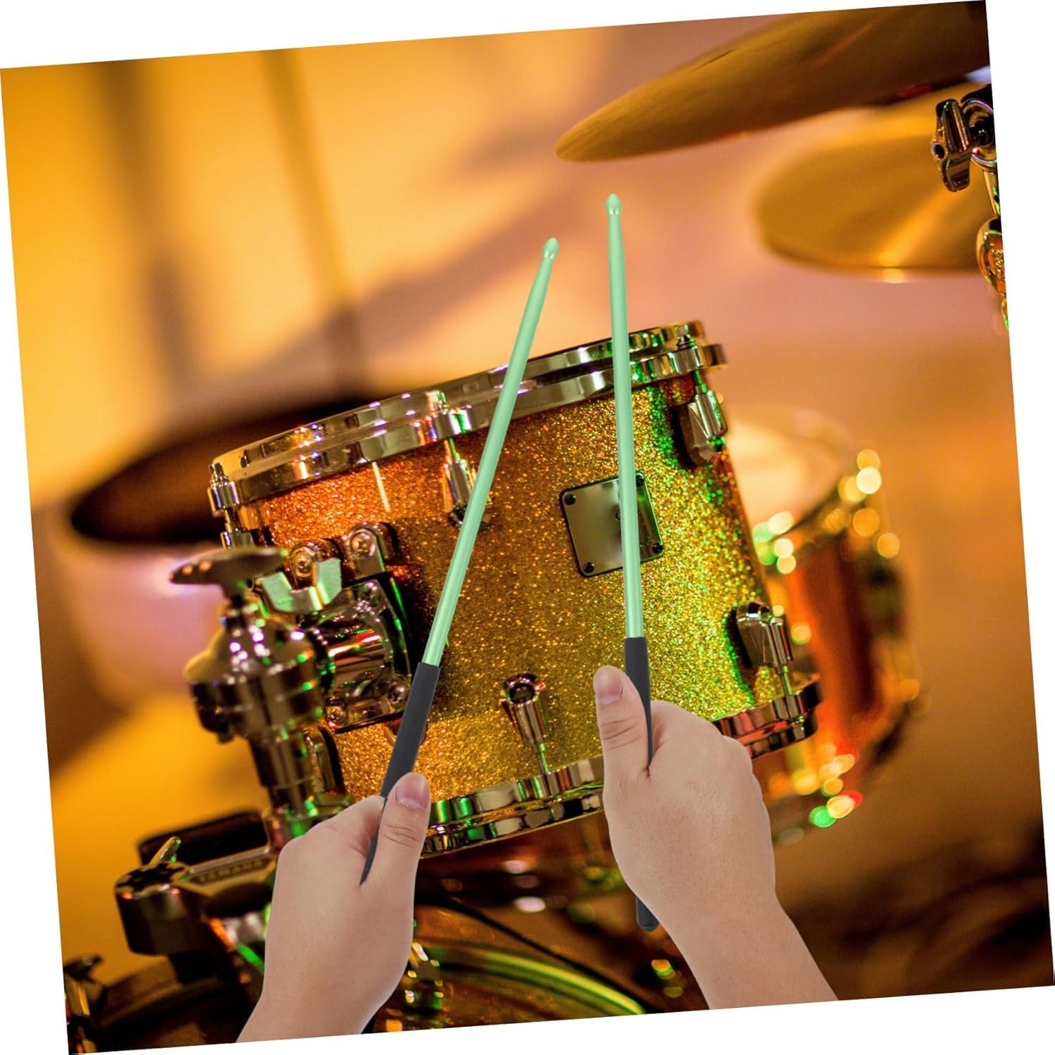 Close-up of a person holding drumsticks in front of a glittery drum set with a warm, blurred background.