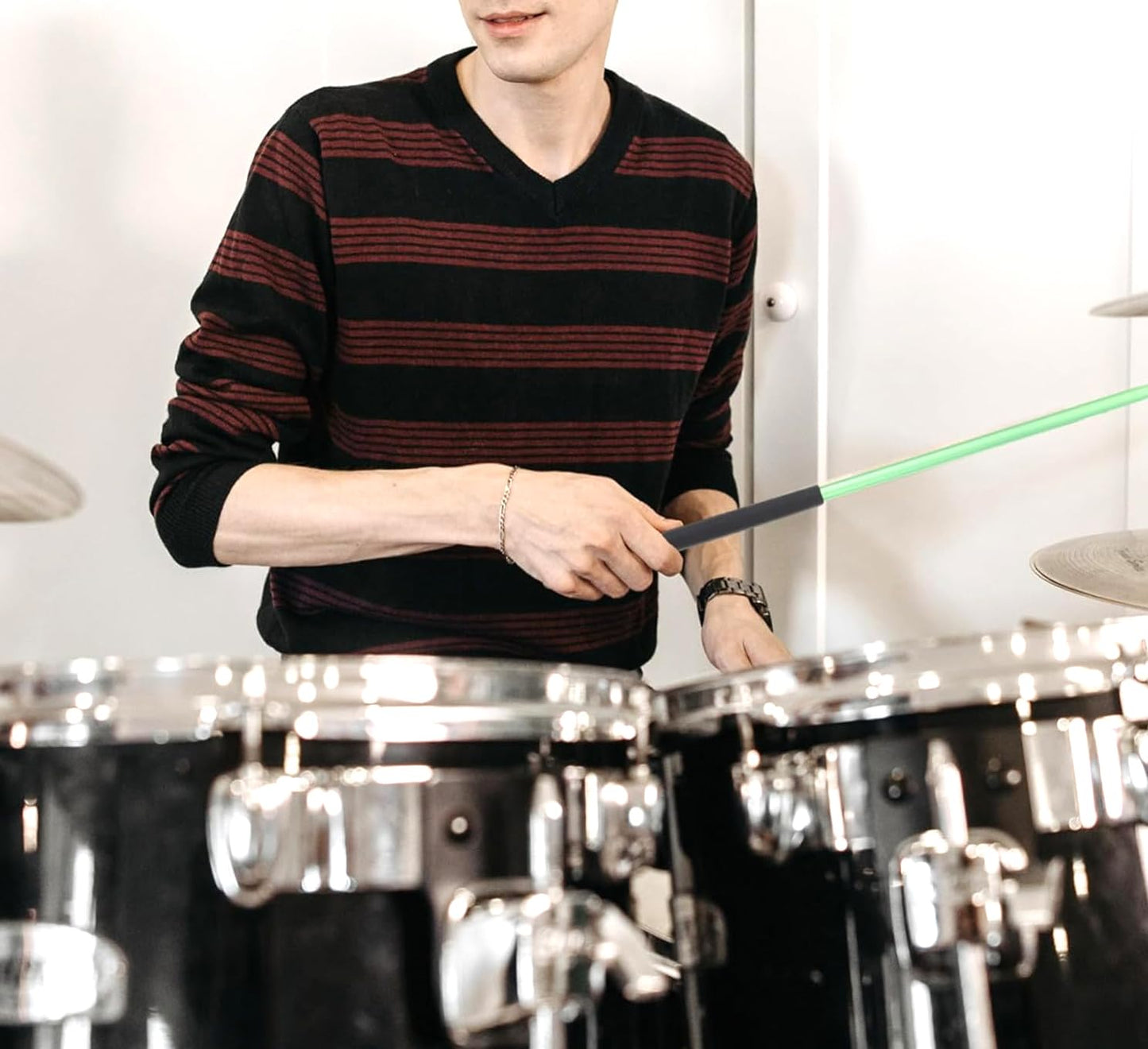 Person playing drums with a green laser pointer in a room with drums and a white wall.