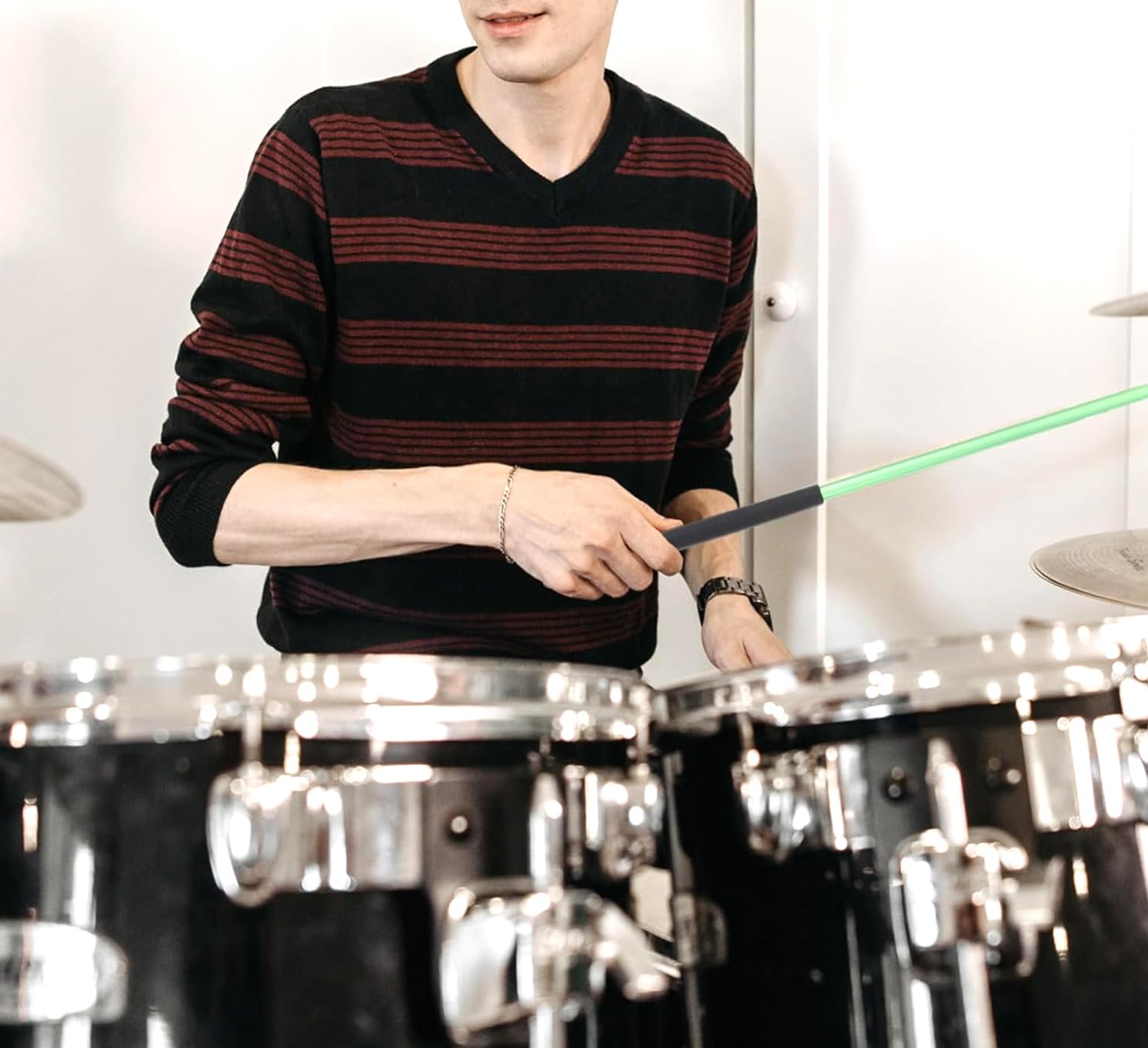 Person playing drums with a green laser pointer in a room with drums and a white wall.