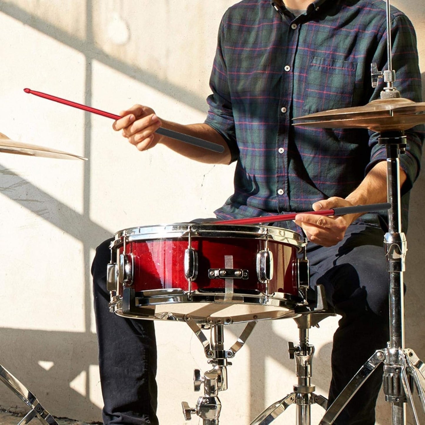 Person playing a red snare drum with drumsticks indoors.