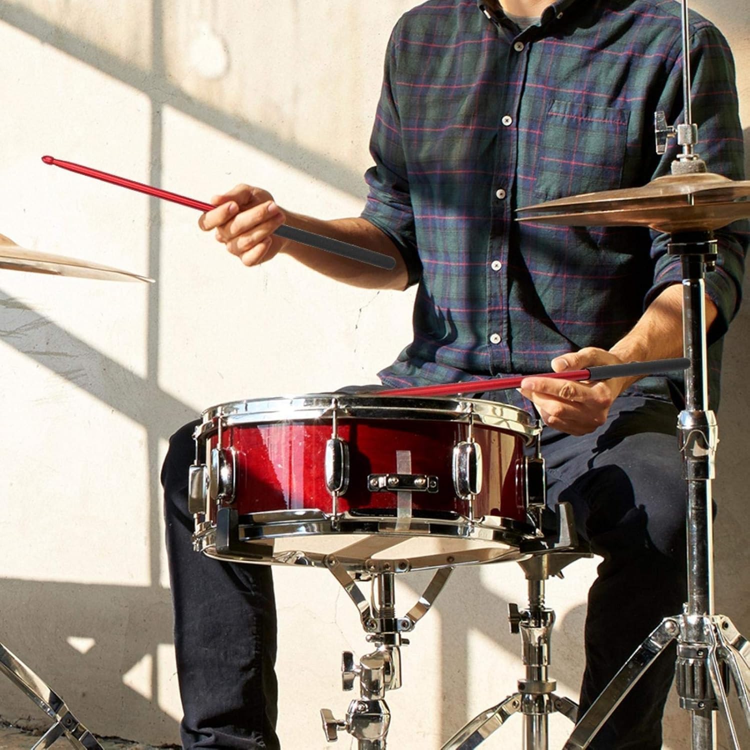 Person playing a red snare drum with drumsticks indoors.